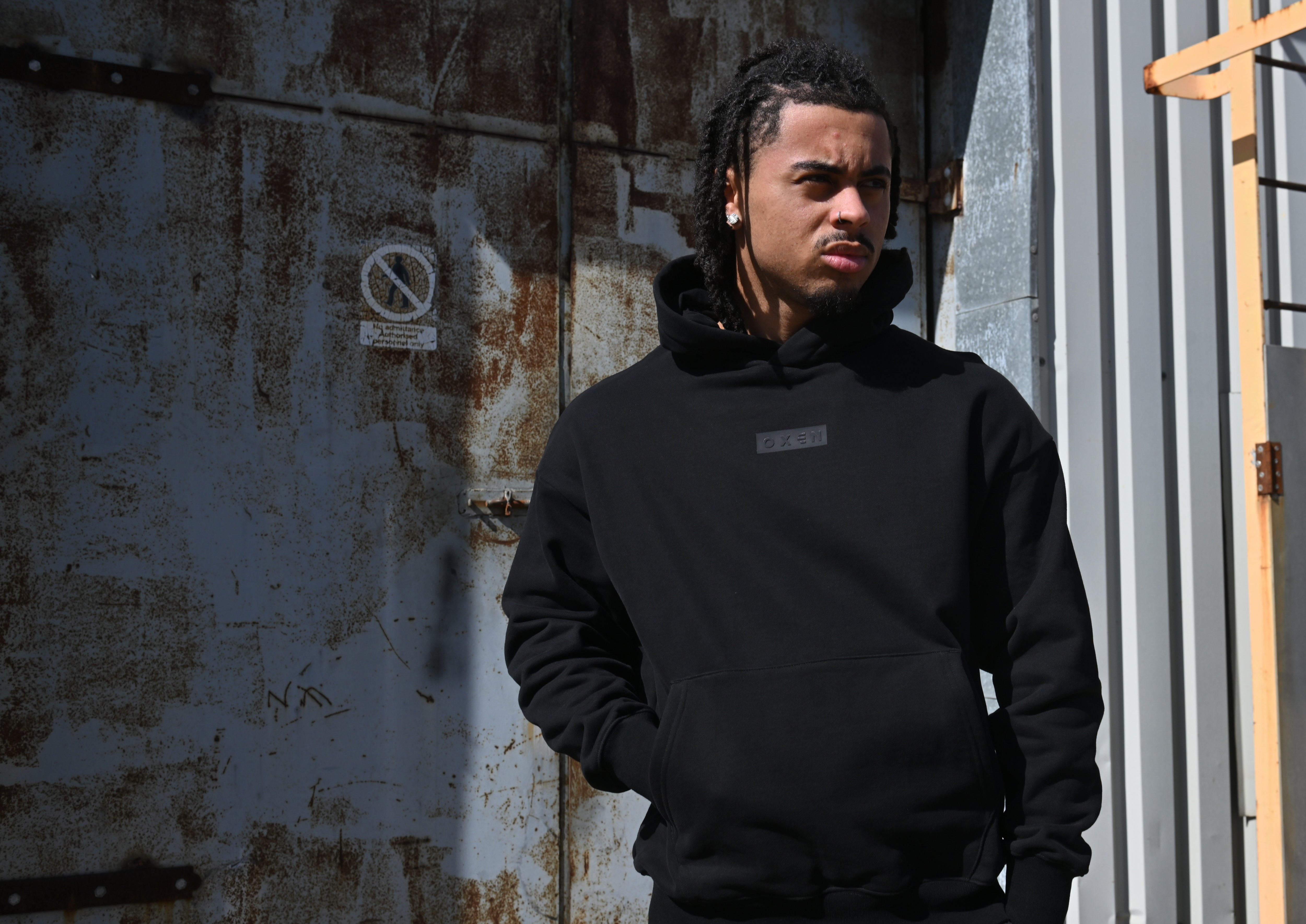 Person wearing a black hoodie standing against a textured wall.
